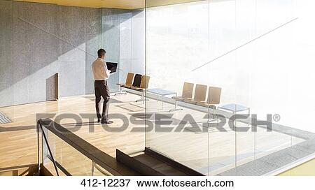 Businessman using laptop in office lobby View Large Photo Image Stock Photo - Businessman using laptop in office lobby. Fotosearch