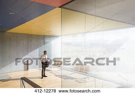 Businessman using laptop in sunny office lobby View Large Photo Image Stock Photo - Businessman using laptop in sunny office lobby. Fotosearch