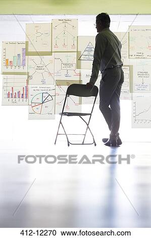 Stock Image - Businessman viewing charts and graphs on office wall. Fotosearch