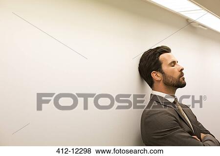 Stock Photo - Businessman with eyes closed leaning against wall. Fotosearch