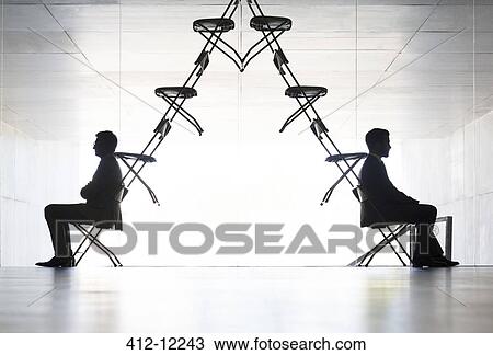 Businessmen sitting at opposite ends of office chair installation art View Large Photo Image Stock Image - Businessmen sitting at opposite ends of office chair installation art. Fotosearch
