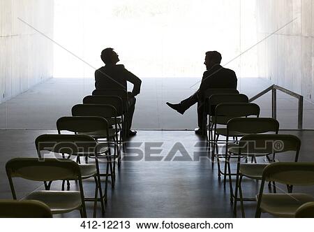 Stock Image - Businessmen talking at chairs in a row. Fotosearch