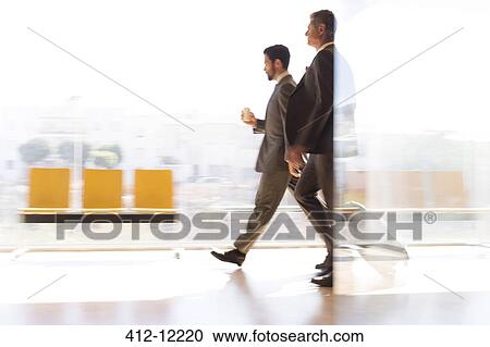 Stock Image - Businessmen walking in airport corridor. Fotosearch
