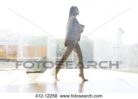Stock Photo - Businesswoman pulling suitcase in airport corridor. Fotosearch