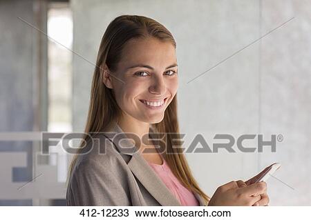 Stock Image - Businesswoman using cell phone in office. Fotosearch