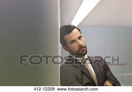 Stock Photo - Serious businessman leaning against office wall. Fotosearch