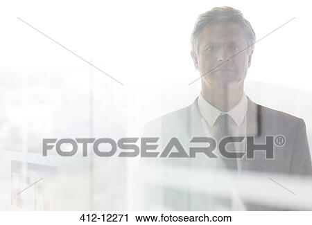 Stock Image - Serious businessman standing at office window. Fotosearch