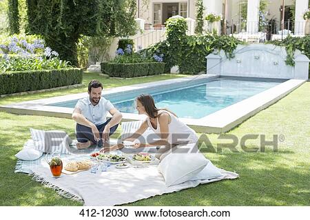 Stock Image - Couple enjoying picnic by pool. Fotosearch
