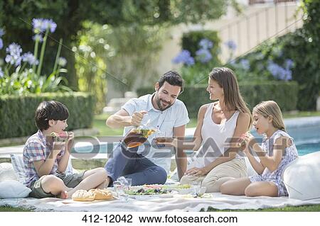 Stock Image - Family enjoying picnic at poolside. Fotosearch