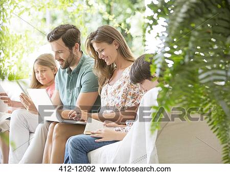 Stock Image - Family reading and using technology on patio. Fotosearch