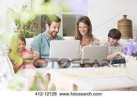 Stock Photograph - Family with laptops, digital tablet and cell phone on patio sofa. Fotosearch