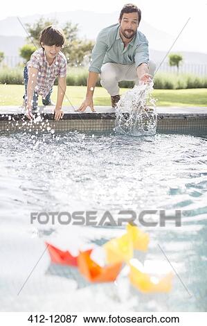 Stock Photo - Father and son racing paper boats in swimming pool. Fotosearch