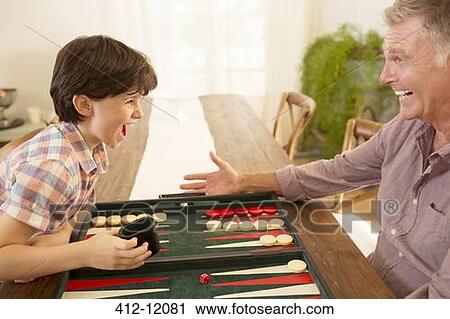 Stock Image - Grandfather and grandson playing backgammon. Fotosearch