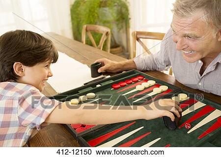 Stock Image - Grandfather and grandson playing backgammon. Fotosearch
