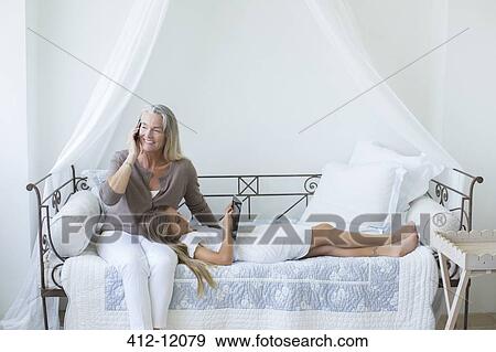 Stock Photo - Grandmother and granddaughter with digital tablet and cell phone on daybed. Fotosearch