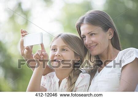 Stock Photograph - Mother and daughter using cell phone outdoors. Fotosearch