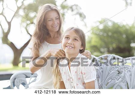 Stock Photo - Mother braiding daughter's hair outdoors. Fotosearch