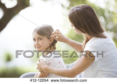 Picture - Mother fixing daughter's hair outdoors. Fotosearch