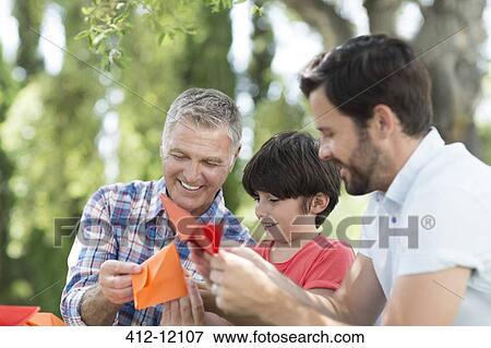 Multi-generation men making origami outdoors View Large Photo Image Stock Photo - Multi-generation men making origami outdoors. Fotosearch
