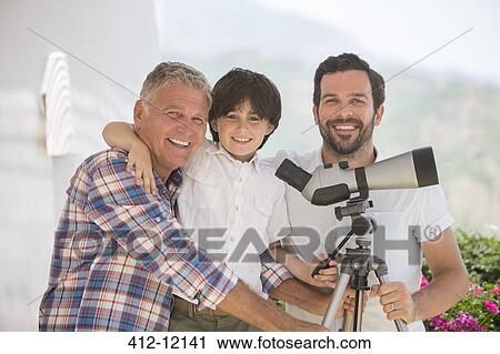 Stock Image - Multi-generation men using telescope outdoors. Fotosearch