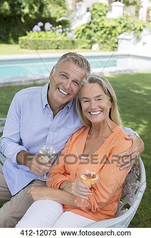 Stock Image - Senior couple drinking wine in backyard. Fotosearch
