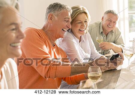 Stock Photo - Senior couples drinking wine and looking at cell phone. Fotosearch