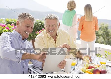 Stock Image - Senior men using digital tablet at patio table. Fotosearch