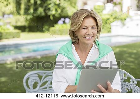 Stock Photograph - Senior woman using digital tablet in backyard. Fotosearch