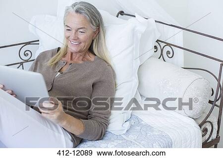 Stock Photo - Senior woman using digital tablet on bed. Fotosearch