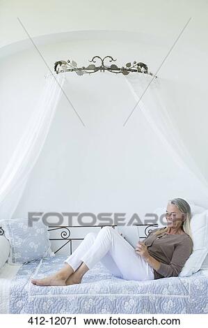 Senior woman with digital tablet relaxing in daybed View Large Photo Image Stock Image - Senior woman with digital tablet relaxing in daybed. Fotosearch