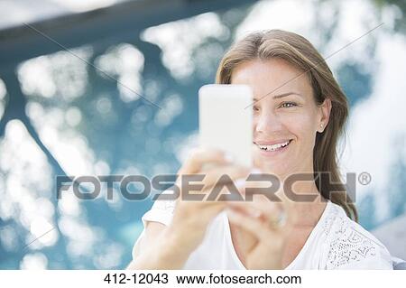 Stock Image - Woman holding cell phone at poolside. Fotosearch