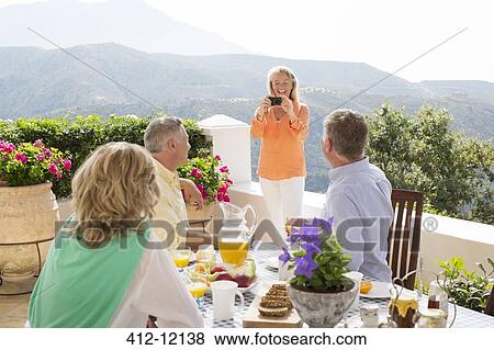 Woman photographing friends at patio table View Large Photo Image Stock Photo - Woman photographing friends at patio table. Fotosearch