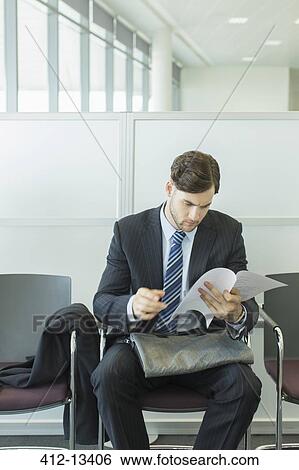 Businessman looking at resume in waiting area View Large Photo Image Stock Photograph - Businessman looking at resume in waiting area. Fotosearch