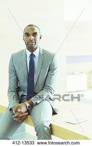 Businessman sitting on desk in office View Large Photo Image Stock Image - Businessman sitting on desk in office. Fotosearch