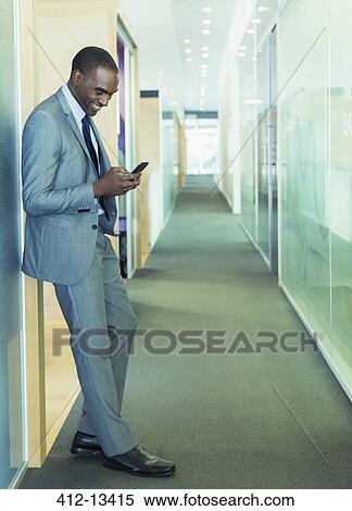 Stock Photography - Businessman using cell phone in office corridor. Fotosearch