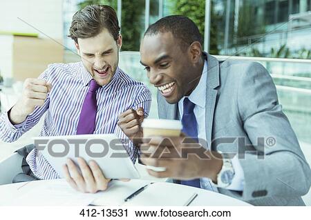 Stock Image - Businessmen cheering at digital tablet. Fotosearch