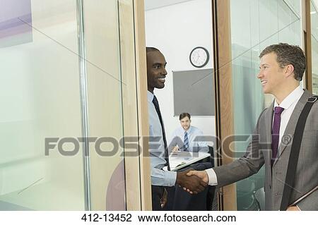 Stock Image - Businessmen shaking hands in office. Fotosearch