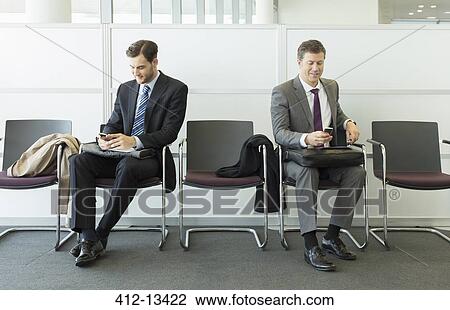 Stock Image - Businessmen sitting in waiting area. Fotosearch