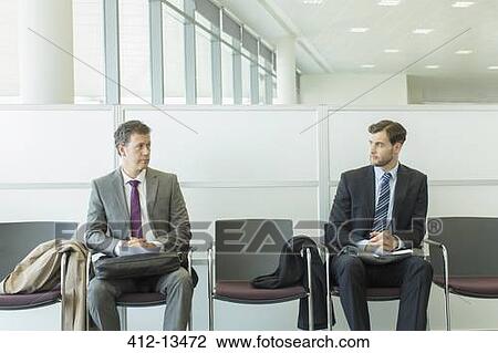 Stock Image - Businessmen sitting in waiting area. Fotosearch