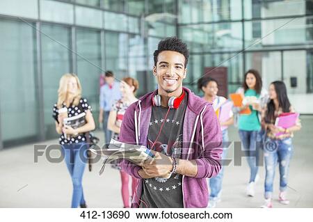 Stock Image - Smiling university student carrying books. Fotosearch