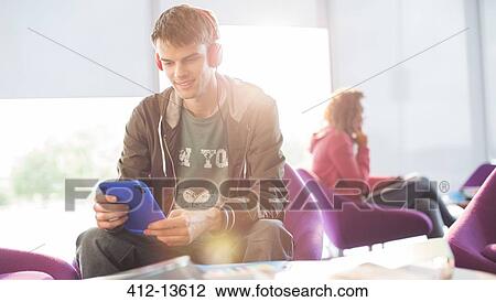 Stock Image - University student listening to headphones in lounge. Fotosearch