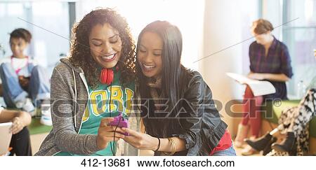 Stock Image - University students using cell phone in lounge. Fotosearch
