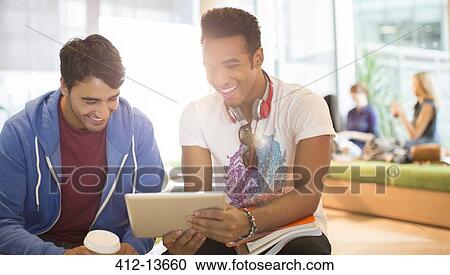 Stock Image - University students using digital tablet in lounge. Fotosearch