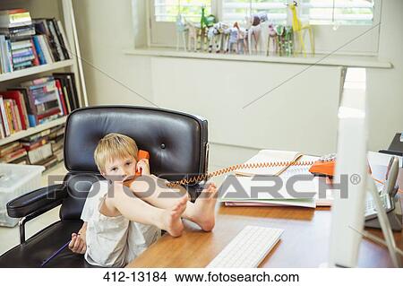 Picture - Boy talking on phone in home office. Fotosearch