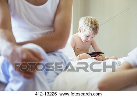 Stock Photograph - Boy using digital tablet on bed. Fotosearch