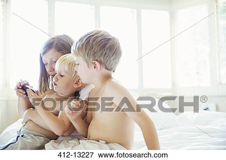 Stock Photo - Children using cell phone on bed. Fotosearch