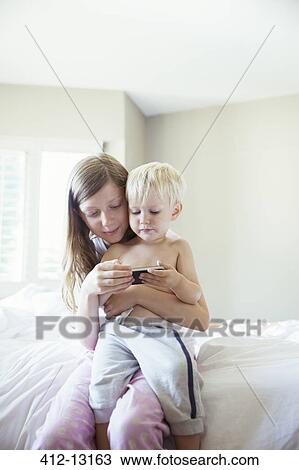 Children using cell phone together on bed View Large Photo Image Stock Image - Children using cell phone together on bed. Fotosearch