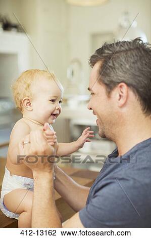 Stock Image - Father and baby laughing in kitchen. Fotosearch