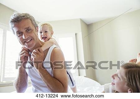 Picture - Father and children playing on bed. Fotosearch
