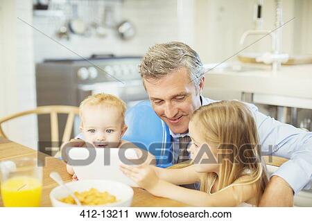 Stock Image - Father and children using digital tablet at table. Fotosearch